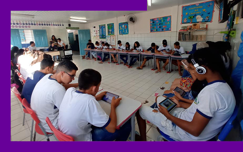Imagem mostra um grupo de estudantes em sala de aula utilizando tablets e fones de ouvido