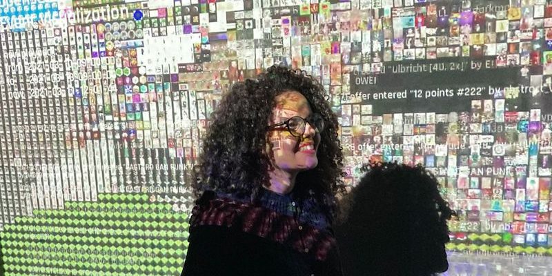 A criadora do projeto Poesia Compilada, Soraya Roberta, aparece com as luzes de um projetor que projeta alguns de seus poemas feitos com algoritmos.