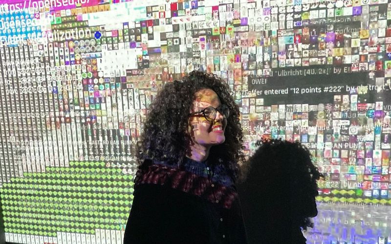 A criadora do projeto Poesia Compilada, Soraya Roberta, aparece com as luzes de um projetor que projeta alguns de seus poemas feitos com algoritmos.