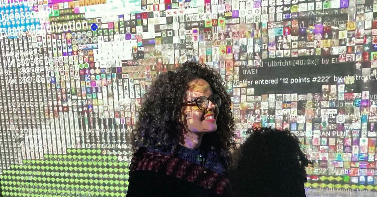 A criadora do projeto Poesia Compilada, Soraya Roberta, aparece com as luzes de um projetor que projeta alguns de seus poemas feitos com algoritmos.