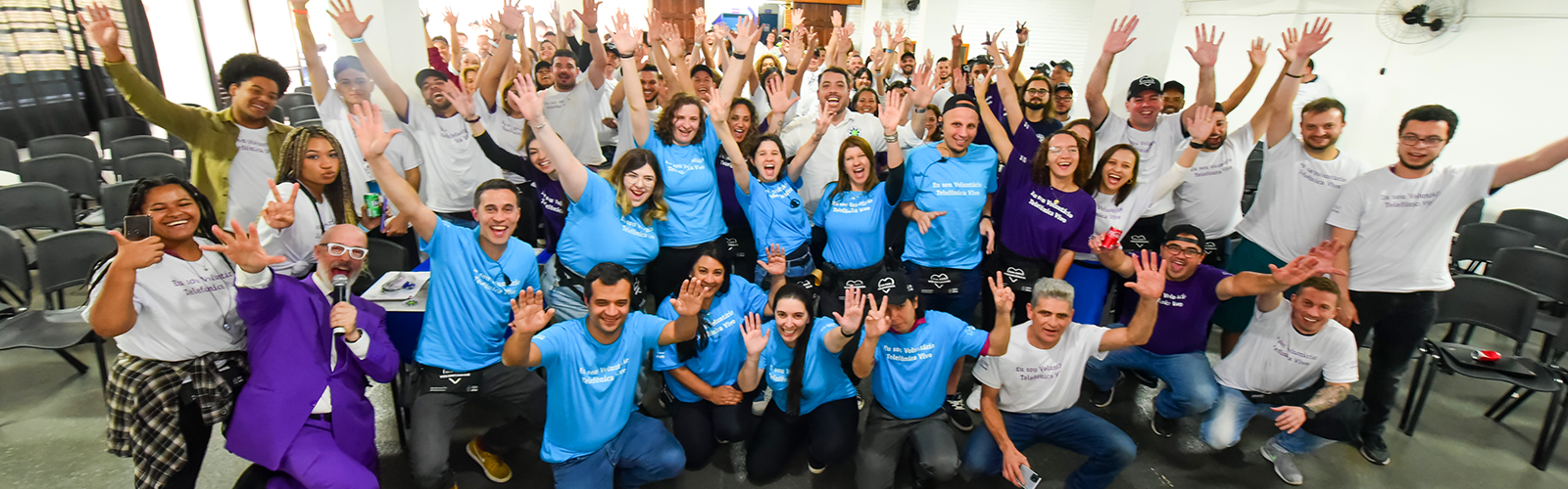 Imagem mostra um grupo com cerca de cem voluntários, entre homens e mulheres, com os braços erguidos e felizes posando para a foto.