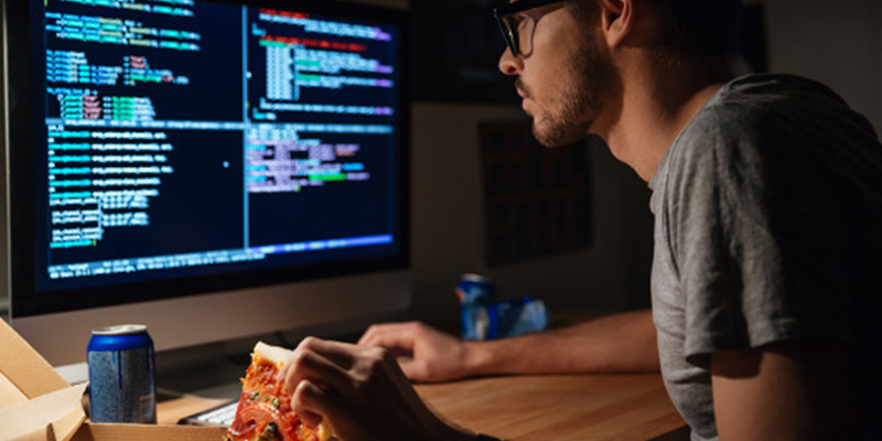 jovem diante de telas e debruçado sobre o teclado. Imagem denota que ele vai começar a programar.