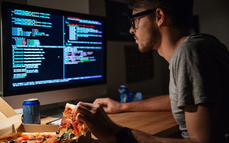 jovem diante de telas e debruçado sobre o teclado. Imagem denota que ele vai começar a programar.