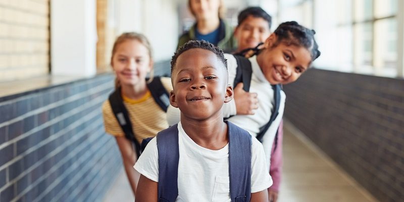 Estudantes representando diversidade étnico-racial posam de maneira intercalada no corredor da escola.