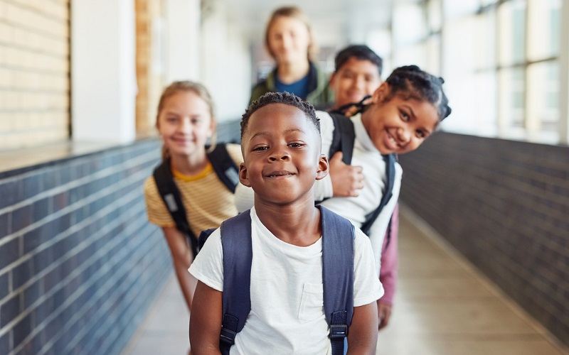 Estudantes representando diversidade étnico-racial posam de maneira intercalada no corredor da escola.