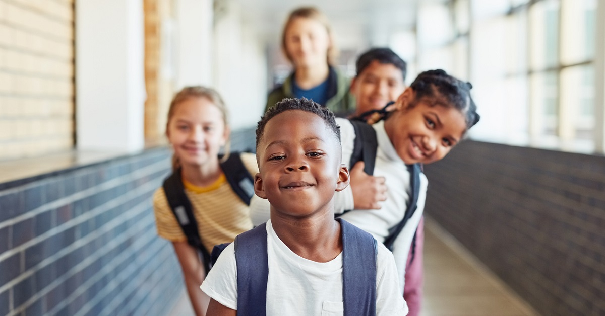Estudantes representando diversidade étnico-racial posam de maneira intercalada no corredor da escola.