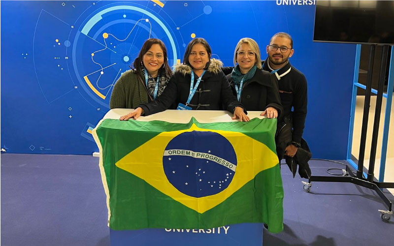 Imagem mostra quatro professores, três mulheres e um homem, em pé, segurando a bandeira do Brasil. Ao fundo se vê um fundo azul com o logotipo do evento enlightED 2022.