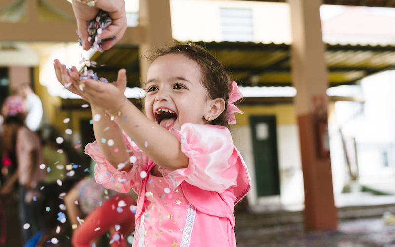 Menina joga confete para cima em festa de carnaval na escola.