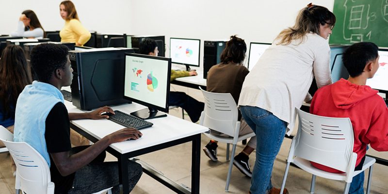 Em sala de informática, estudantes utilizam computadores para analisar dados e gráficos.