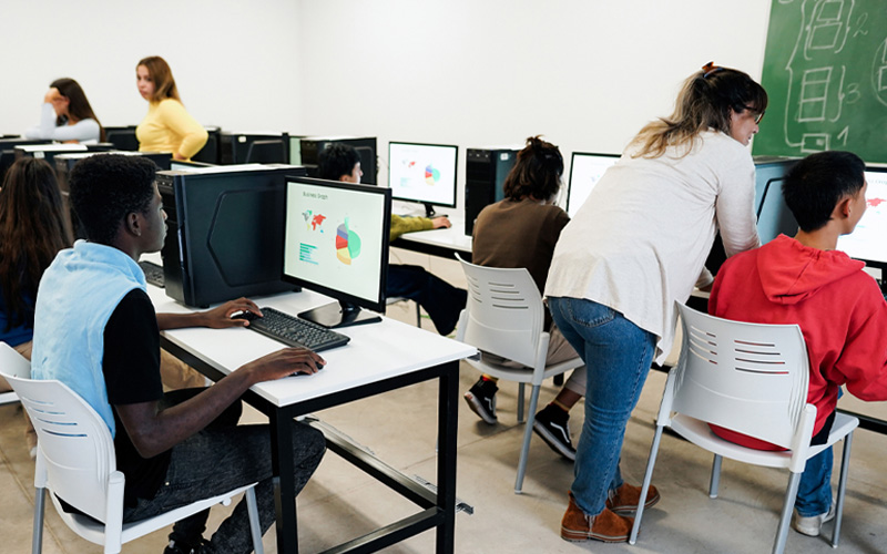 Em sala de informática, estudantes utilizam computadores para analisar dados e gráficos.