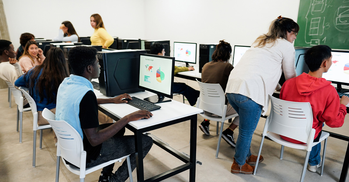 Em sala de informática, estudantes utilizam computadores para analisar dados e gráficos.