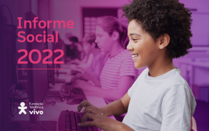 Imagem mostra um menino negro utilizando um computador em sala de aula com outros estudantes ao fundo
