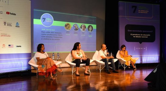 Imagem mostra o palco do congresso da Jeduca com quatro palestrantes, um homem branco, duas mulheres brancas e uma mulher negra. Todos estão sentados