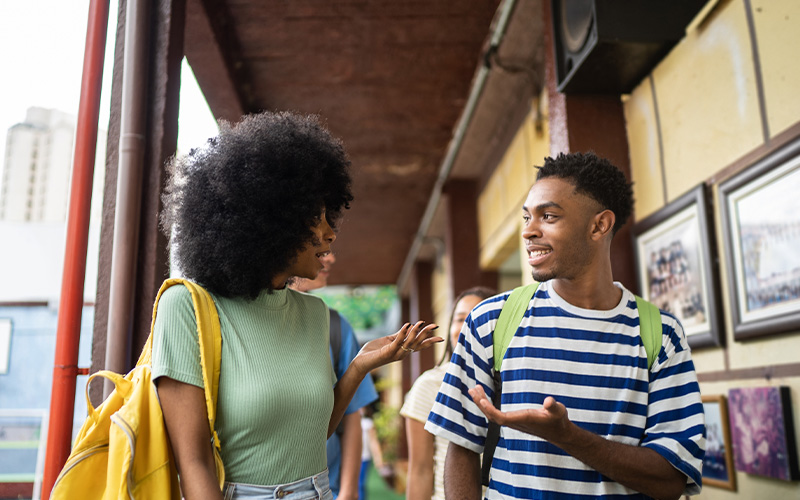 Imagem mostra dois jovens estudantes negros conversando e andando por um corredor.
