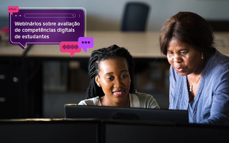 Imagem mostra uma educadora e uma estudante em sala de aula, utilizando computador, ambas são negras. A professora está mostrando algo para a aluna na tela do computador