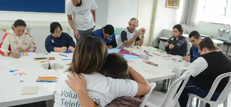 Mulher abraça menino durante atividade no CENHA, onde voluntários do Vacaciones Solidárias ensinaram programação para pessoas com deficiência intelectual.