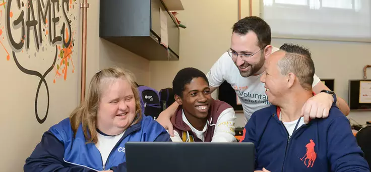 Três jovens sorriem durante atividade no CENHA, onde voluntários do Vacaciones Solidárias ensinaram programação para pessoas com deficiência intelectual.