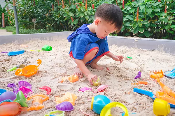 A imagem mostra uma criança brincando com objetos dentro de um tanque de areia
