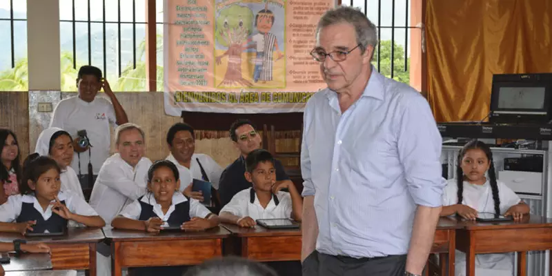 Na imagem, César Alierta está no ambiente de uma escola, ao fundo podemos ver vários alunos sentados em suas mesas