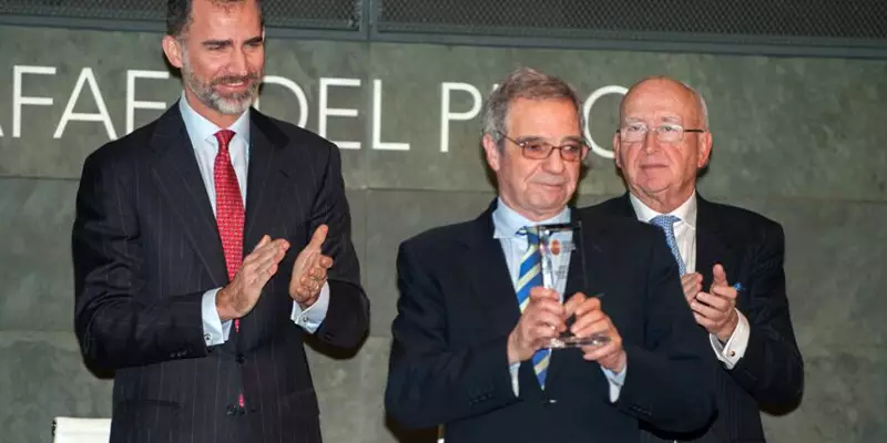 Na imagem, César Alierta está segurando um troféu, em um palco, ao lado de dois homens